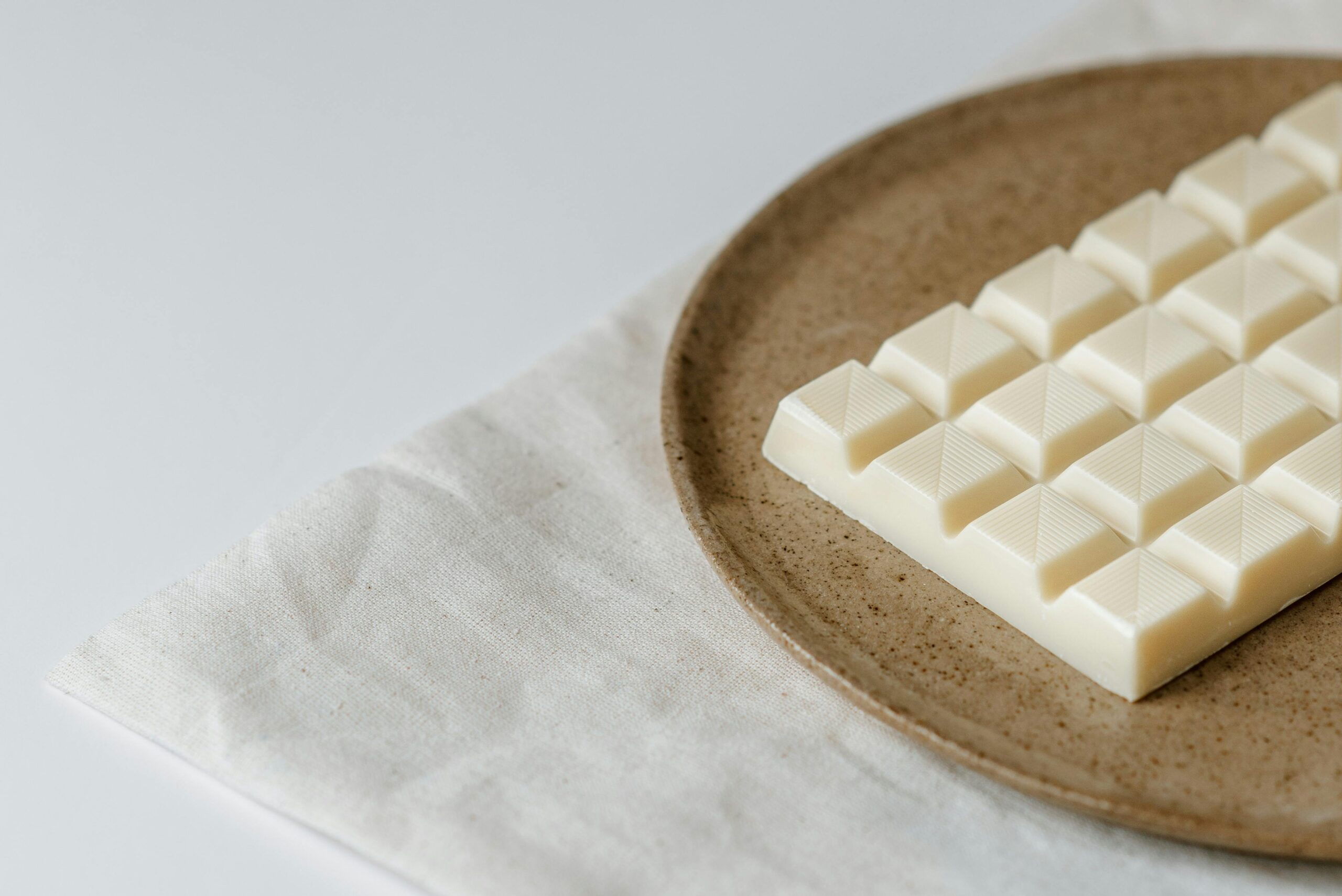 High angle of modern ceramic plate with bar of white chocolate on table